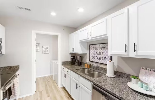 kitchen with light wood finished floors, visible vents, dark stone countertops, white cabinets, and a sink