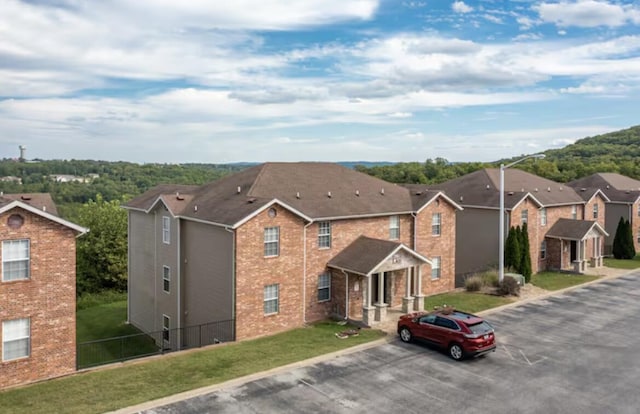 exterior space featuring brick siding, uncovered parking, a front lawn, and fence