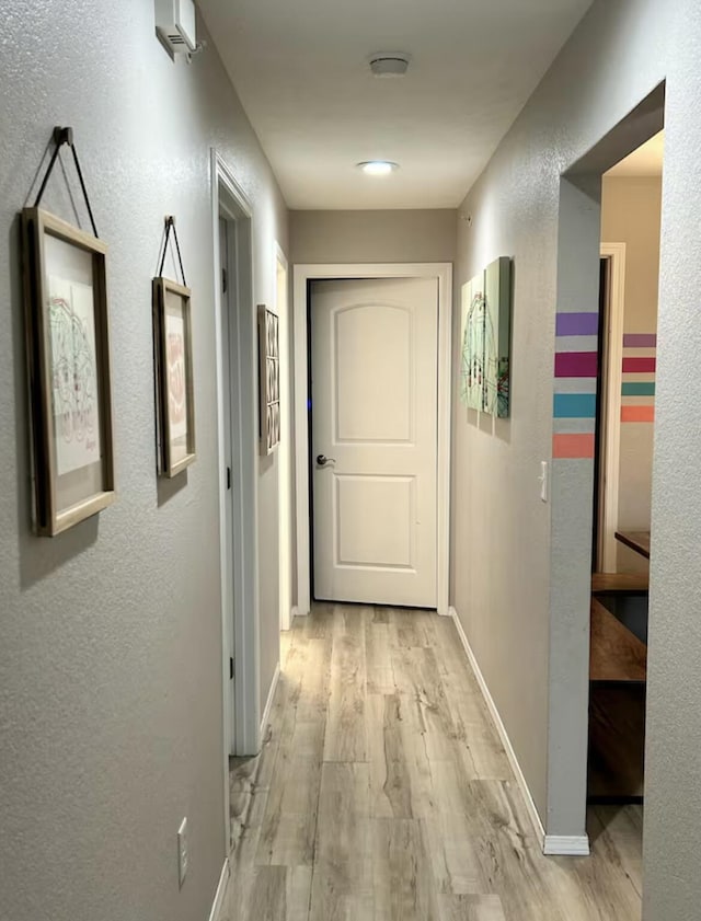 corridor with light wood-type flooring, baseboards, and a textured wall