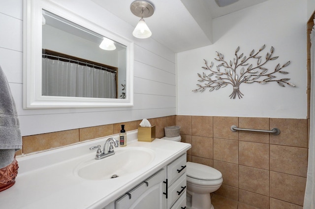 full bath featuring toilet, tile walls, wainscoting, and vanity