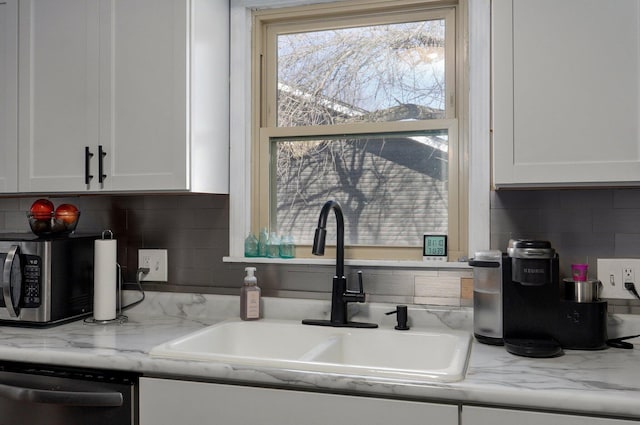 kitchen with a sink, white cabinetry, stainless steel appliances, decorative backsplash, and light stone countertops