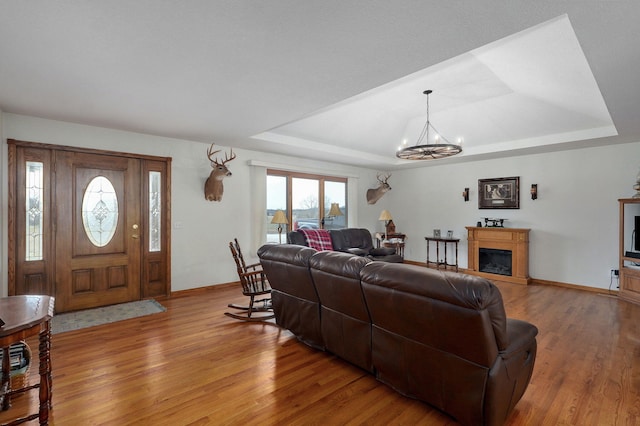 living room with a tray ceiling, wood finished floors, baseboards, and a glass covered fireplace