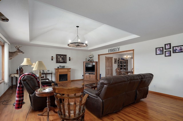 living room with an inviting chandelier, a tray ceiling, and wood finished floors