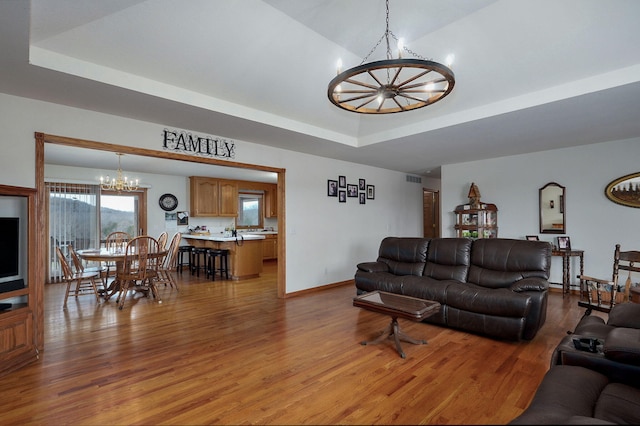 living area with a raised ceiling, a notable chandelier, light wood-style floors, and baseboards