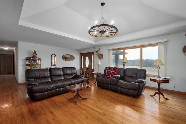 living room featuring a tray ceiling, baseboards, light wood-type flooring, and a chandelier