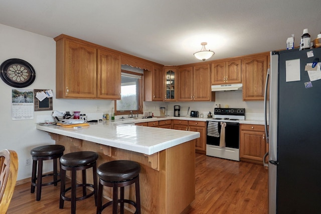 kitchen featuring wood finished floors, a peninsula, freestanding refrigerator, electric stove, and under cabinet range hood