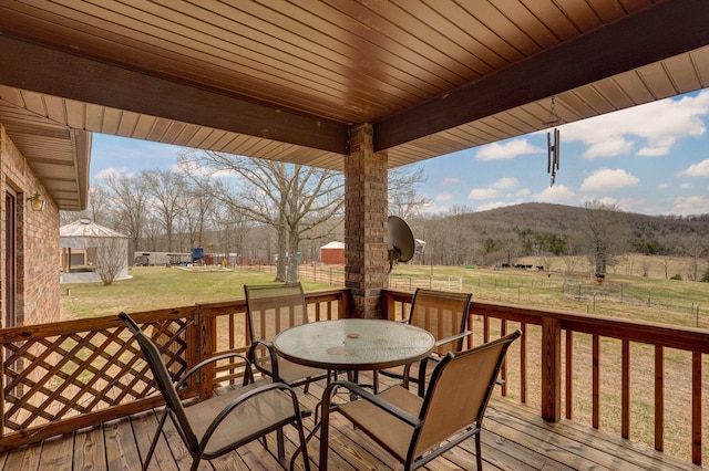 deck with outdoor dining area, a yard, and a rural view