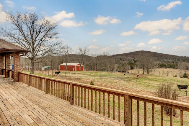 deck featuring a rural view, fence, a yard, an outdoor structure, and an outbuilding