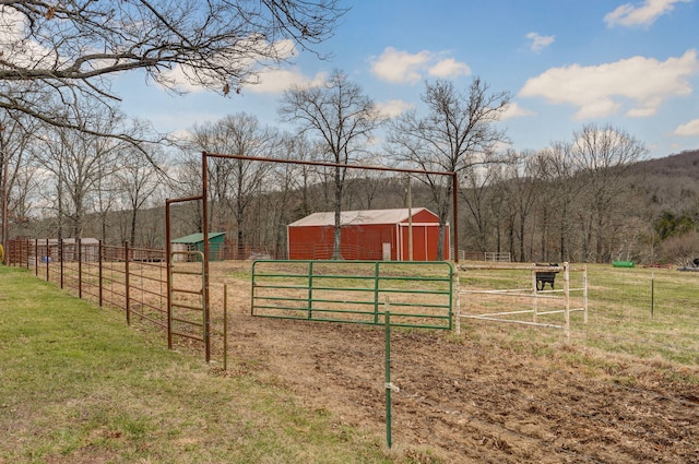 view of yard featuring an outbuilding, a rural view, a wooded view, and fence