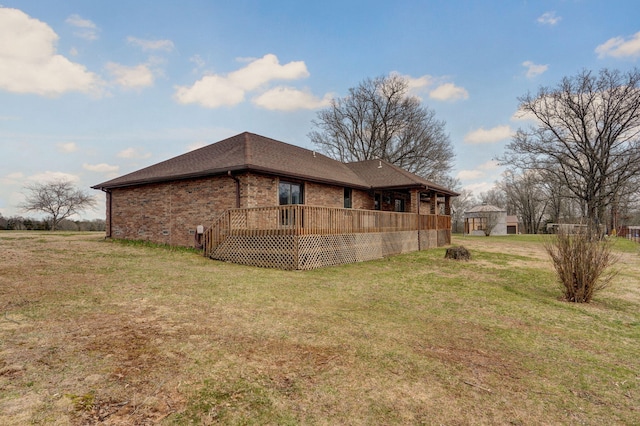 rear view of house featuring brick siding, roof with shingles, and a lawn