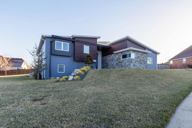 view of front of property with stone siding, a front yard, and fence