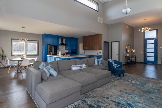 living area with visible vents, a high ceiling, a chandelier, and dark wood finished floors