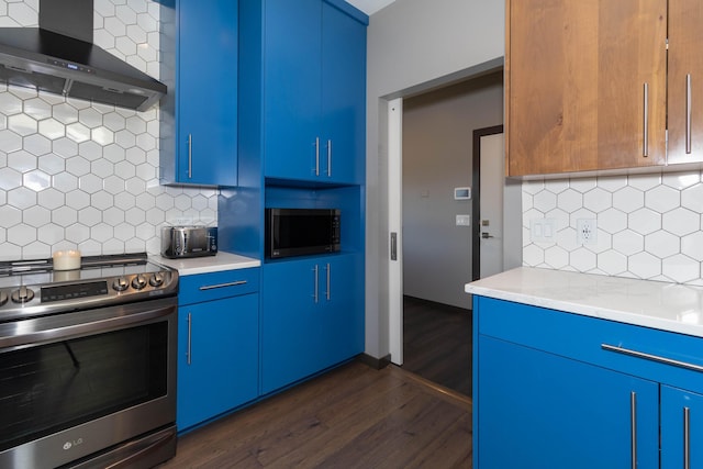 kitchen with blue cabinetry, stainless steel appliances, light countertops, and wall chimney range hood