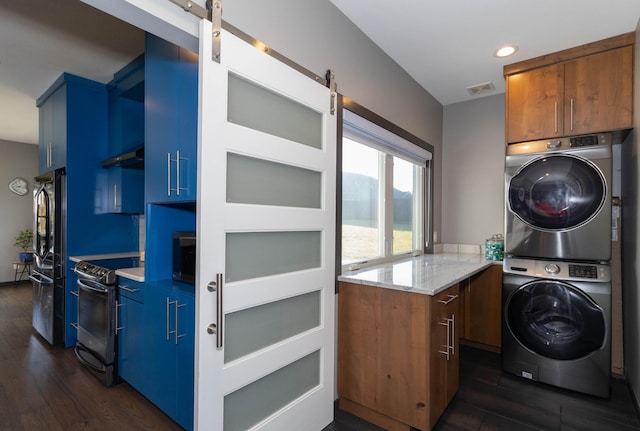 laundry area featuring visible vents, dark wood-style floors, stacked washing maching and dryer, a barn door, and laundry area