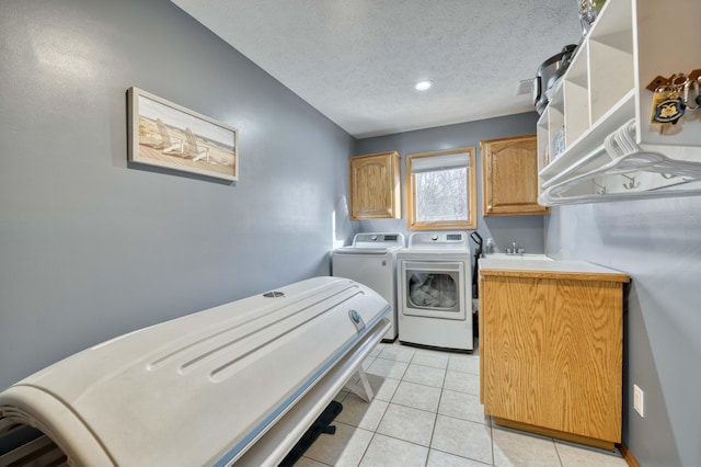 laundry area featuring light tile patterned floors, cabinet space, a textured ceiling, independent washer and dryer, and a sink