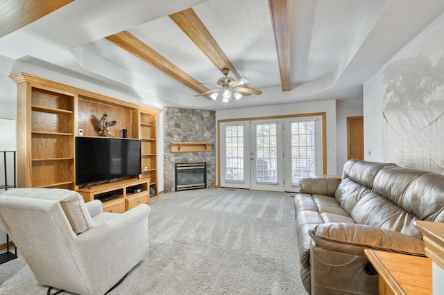 living room with beamed ceiling, light carpet, french doors, a stone fireplace, and ceiling fan