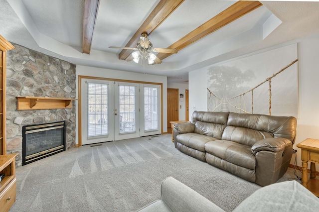 living area with beamed ceiling, a ceiling fan, french doors, carpet, and a stone fireplace