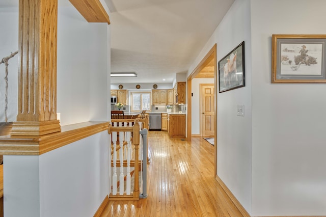 hall featuring light wood-type flooring, an upstairs landing, and baseboards