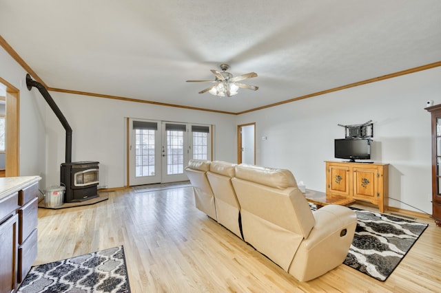 living area with baseboards, light wood-style flooring, french doors, a wood stove, and a ceiling fan