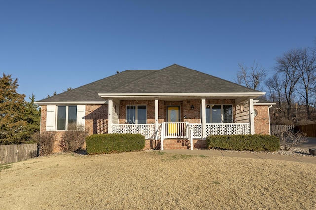 view of front of house featuring fence, brick siding, a porch, and a shingled roof