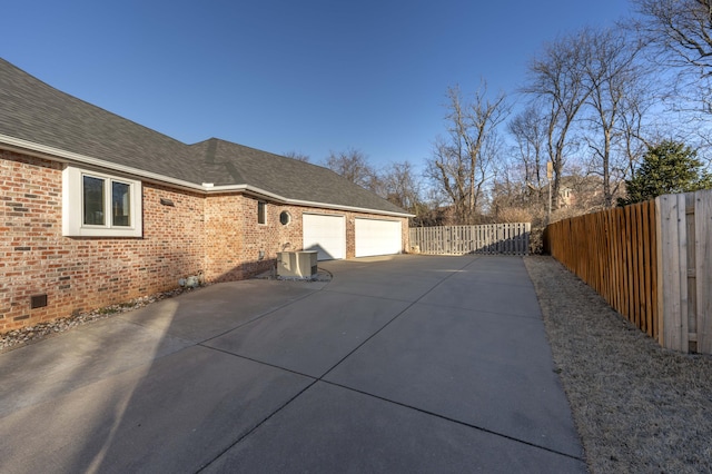 view of home's exterior with a garage, driveway, a shingled roof, crawl space, and brick siding