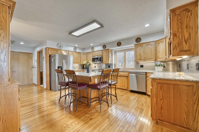 kitchen featuring a breakfast bar, light wood-style flooring, a sink, tasteful backsplash, and appliances with stainless steel finishes