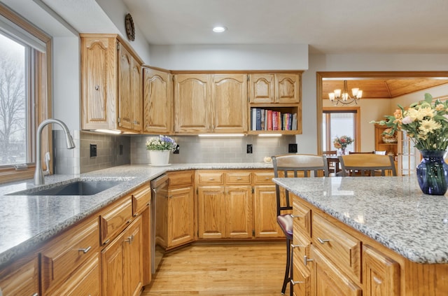 kitchen with light stone counters, a sink, decorative backsplash, light wood-style floors, and dishwasher