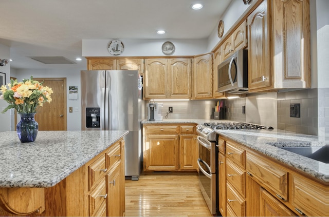 kitchen featuring light stone counters, tasteful backsplash, recessed lighting, appliances with stainless steel finishes, and light wood finished floors