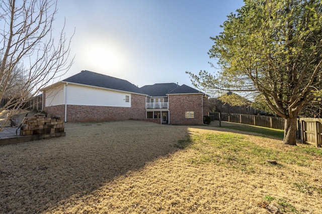 rear view of house featuring brick siding, a lawn, a balcony, and fence