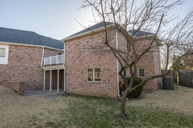 rear view of house featuring a balcony, central air condition unit, a yard, and brick siding