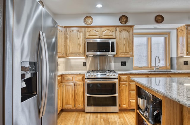 kitchen featuring a sink, light stone counters, tasteful backsplash, appliances with stainless steel finishes, and light wood finished floors