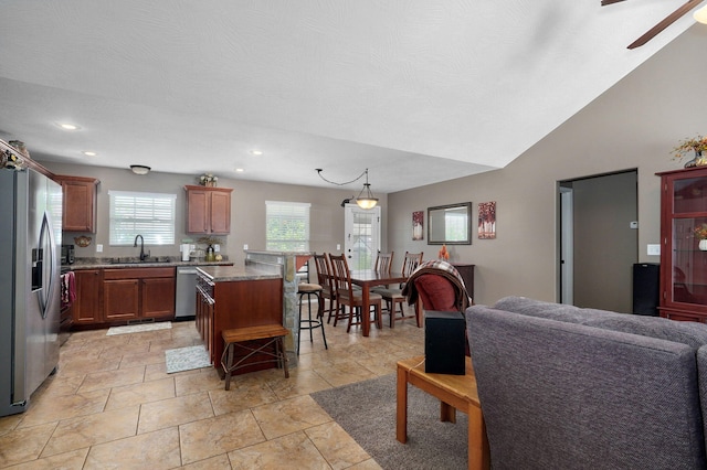 kitchen with open floor plan, a kitchen bar, vaulted ceiling, stainless steel appliances, and a sink