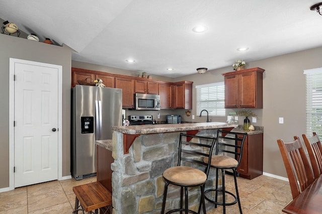 kitchen featuring baseboards, a kitchen bar, recessed lighting, appliances with stainless steel finishes, and brown cabinetry