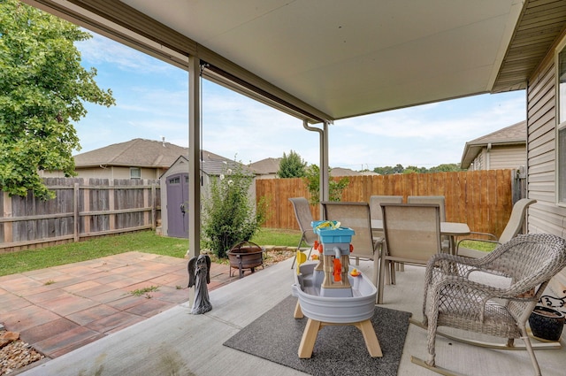 view of patio / terrace featuring outdoor dining space, a fenced backyard, an outdoor structure, a storage unit, and a fire pit