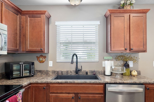 kitchen with brown cabinetry, a sink, stainless steel dishwasher, dark countertops, and range