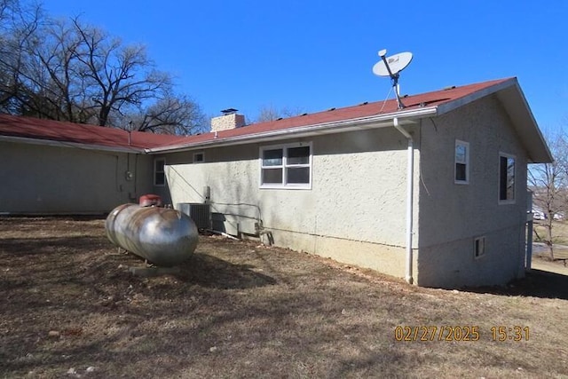 back of house with central AC unit, a chimney, and stucco siding