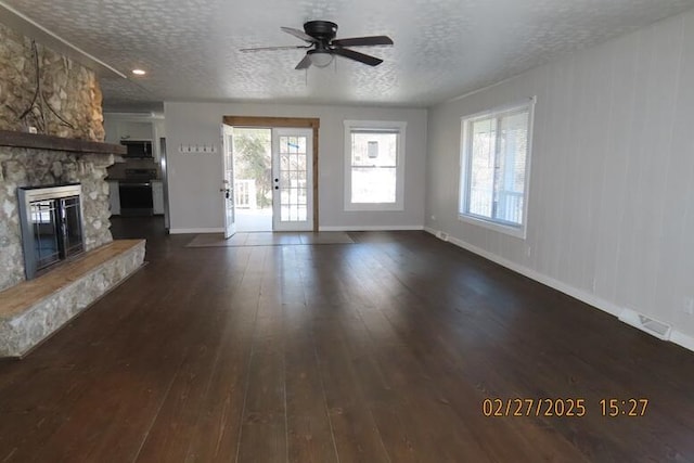 unfurnished living room featuring dark wood finished floors, a stone fireplace, visible vents, and a wealth of natural light