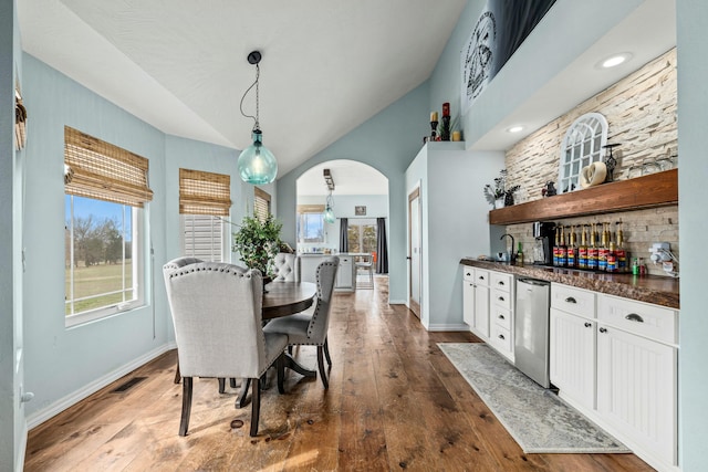 dining space featuring arched walkways, plenty of natural light, baseboards, and hardwood / wood-style flooring