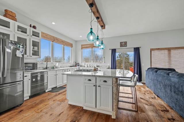 kitchen with light stone countertops, stainless steel appliances, white cabinets, glass insert cabinets, and open floor plan