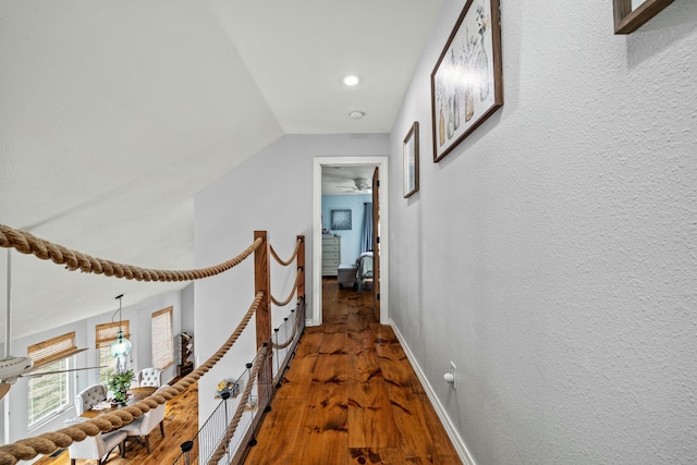 hall with baseboards, lofted ceiling, wood finished floors, and a textured wall