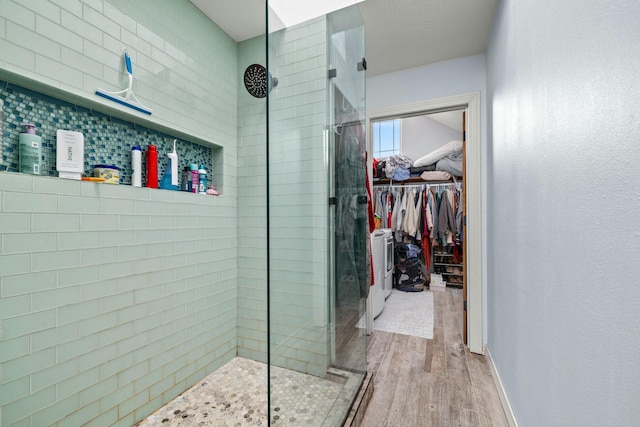 full bathroom featuring a spacious closet, tiled shower, baseboards, and wood finished floors