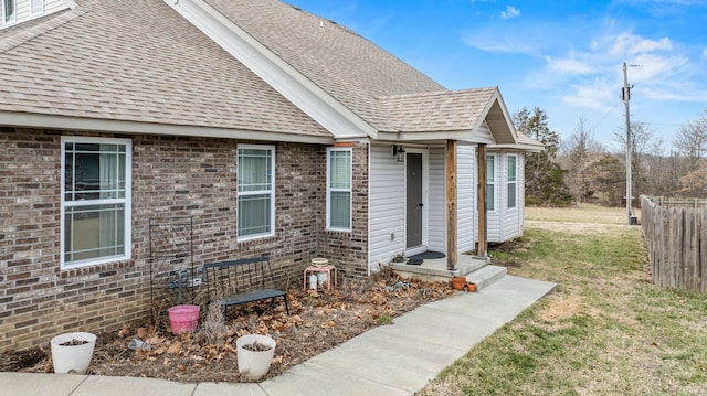 entrance to property featuring fence, a lawn, brick siding, and a shingled roof