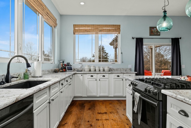 kitchen with a sink, a wealth of natural light, white cabinets, black appliances, and dark wood-style flooring