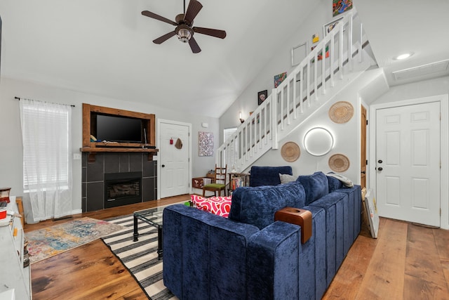 living room featuring ceiling fan, stairs, lofted ceiling, a tile fireplace, and wood finished floors