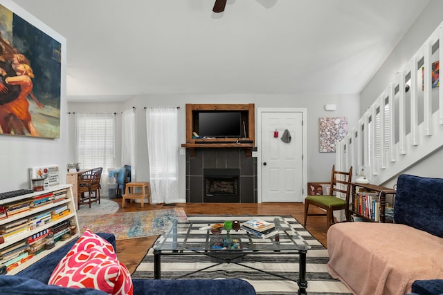 living area featuring a ceiling fan, wood finished floors, stairs, and a tile fireplace