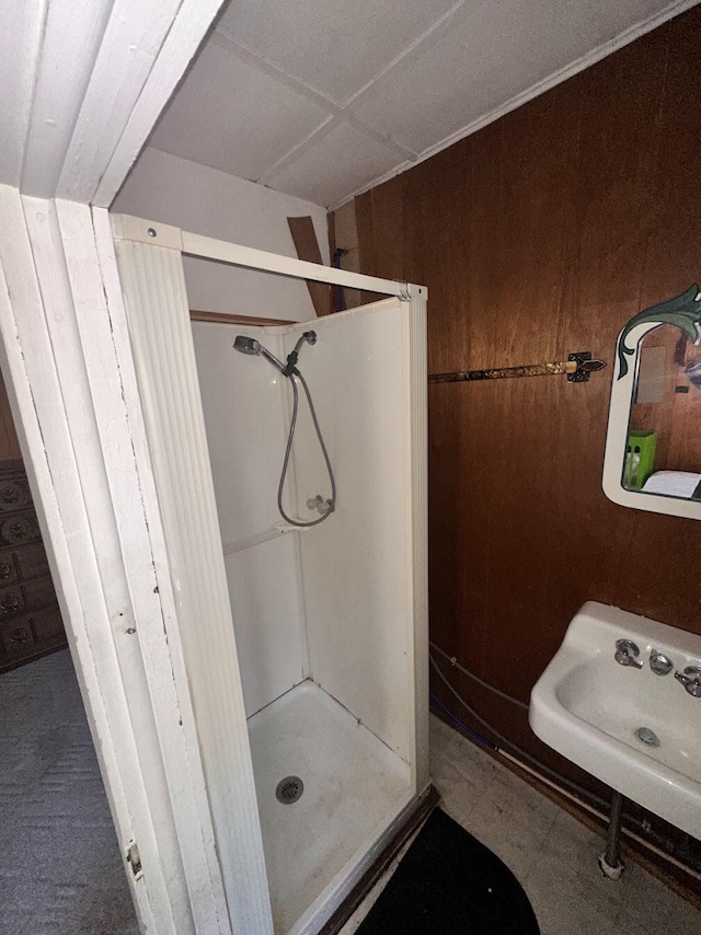 bathroom with wood walls, a stall shower, and a sink