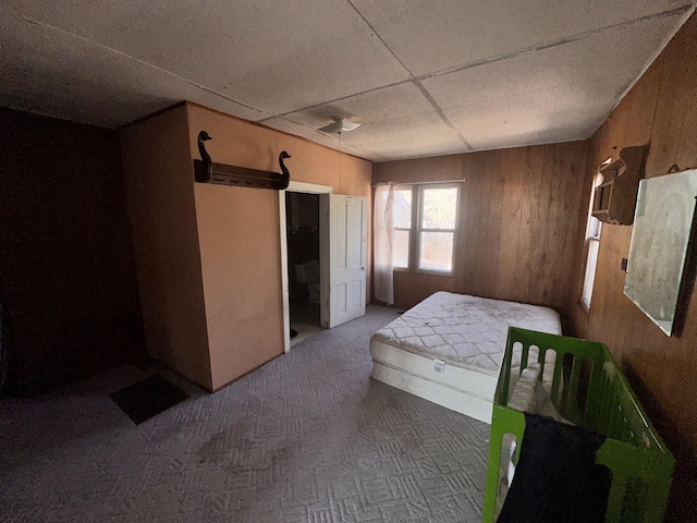 bedroom featuring wooden walls, carpet, and a drop ceiling