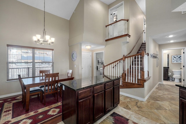 kitchen with an inviting chandelier, a towering ceiling, baseboards, and dark stone countertops