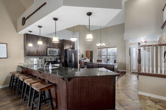 kitchen featuring a towering ceiling, stainless steel appliances, dark brown cabinets, baseboards, and a peninsula