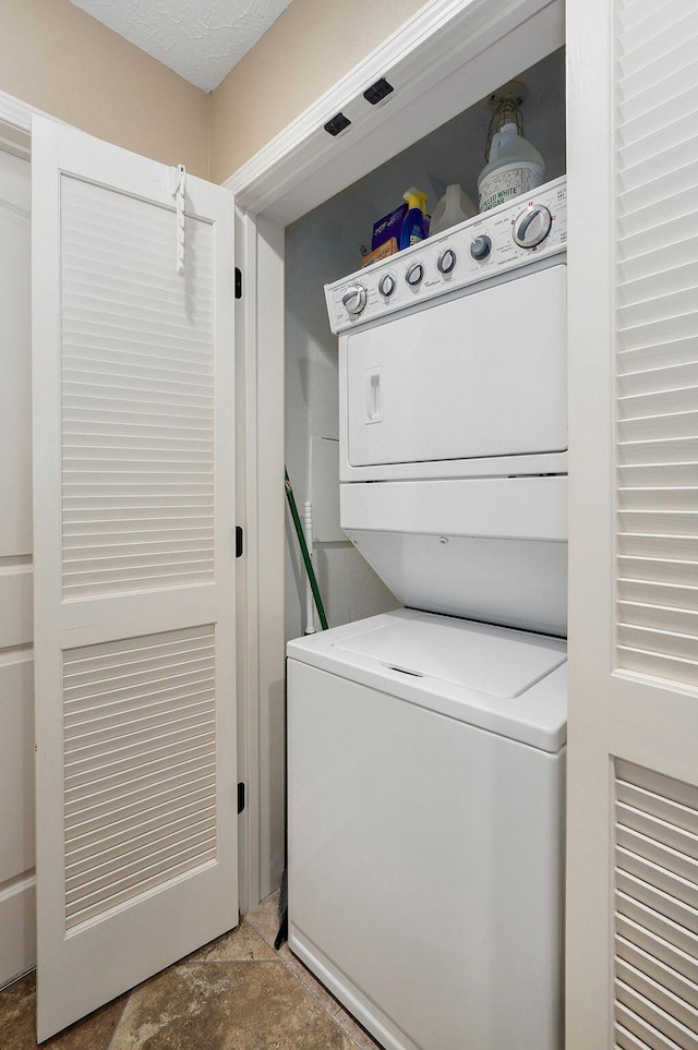 clothes washing area featuring stacked washer and dryer, stone finish floor, and laundry area